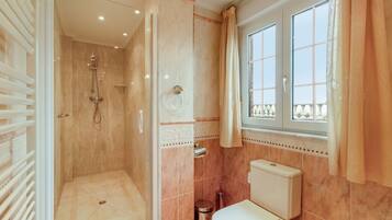 Une salle de bain avec douche, toilettes et une fenêtre avec des rideaux.