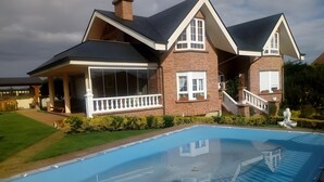 Una casa grande con piscina, un porche cubierto y fachada de ladrillo.
