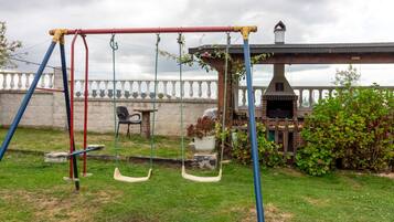 Een achtertuin met een schommel, een barbecue en een stenen muur.