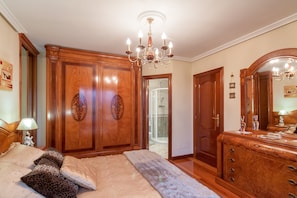 A bedroom with a bed, a wooden wardrobe, a dresser, and a chandelier.