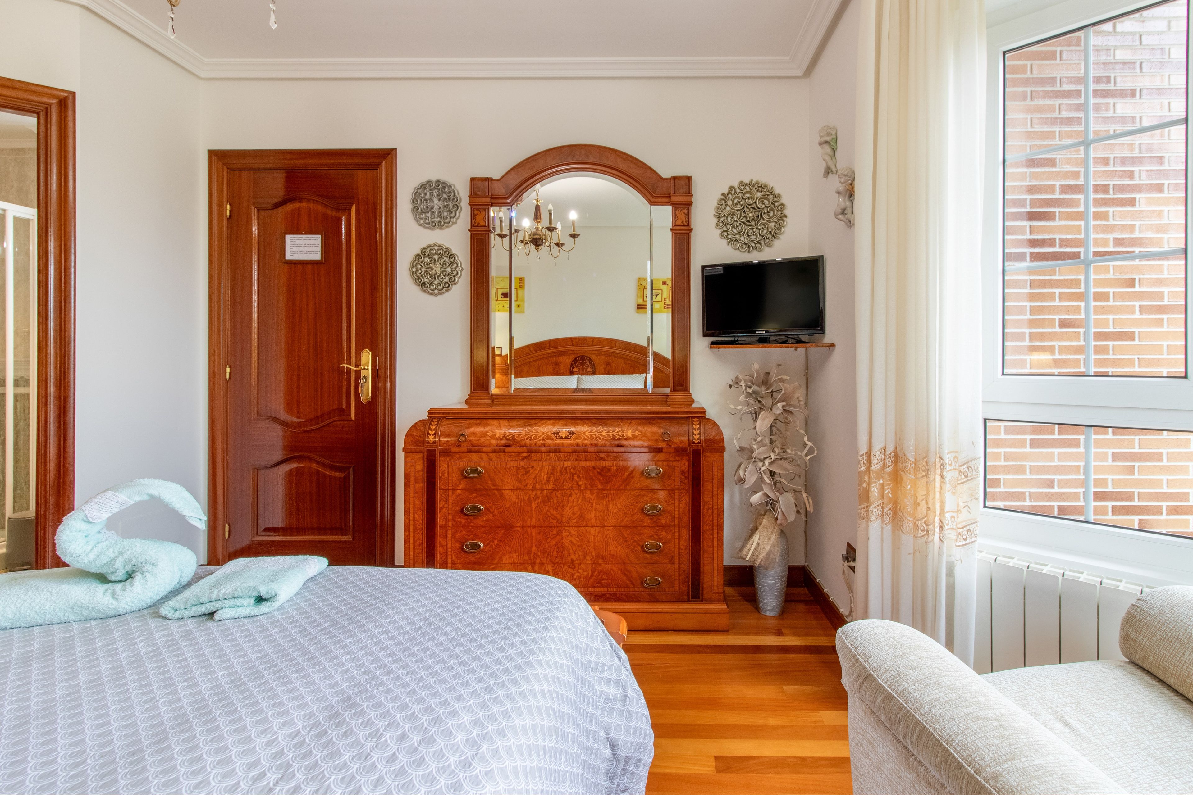 A bedroom with a bed, dresser, mirror, television, and a window with curtains.