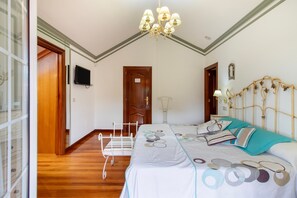 A bedroom with a bed, a bedside table, a television, a chandelier, and a door.