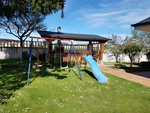 Une aire de jeux avec des balançoires, un toboggan et une cabane couverte.