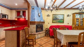 Un coin repas avec une cheminée, des chaises en bois, une table recouverte d’une nappe rouge et une bibliothèque.