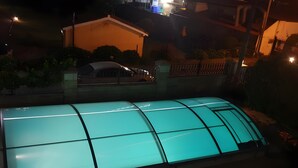 En swimmingpool med en glasvägg runt om, omgiven av ett staket och en byggnad i bakgrunden.