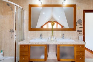 A bathroom with a shower, two sinks, a large mirror, and wooden cabinets.