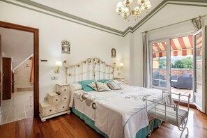 Ein Schlafzimmer mit einem Bett, Nachttischen, einer Kristallleuchtre, einem Fenster mit Aussicht und einer Tür, die zu einer Treppe führt.