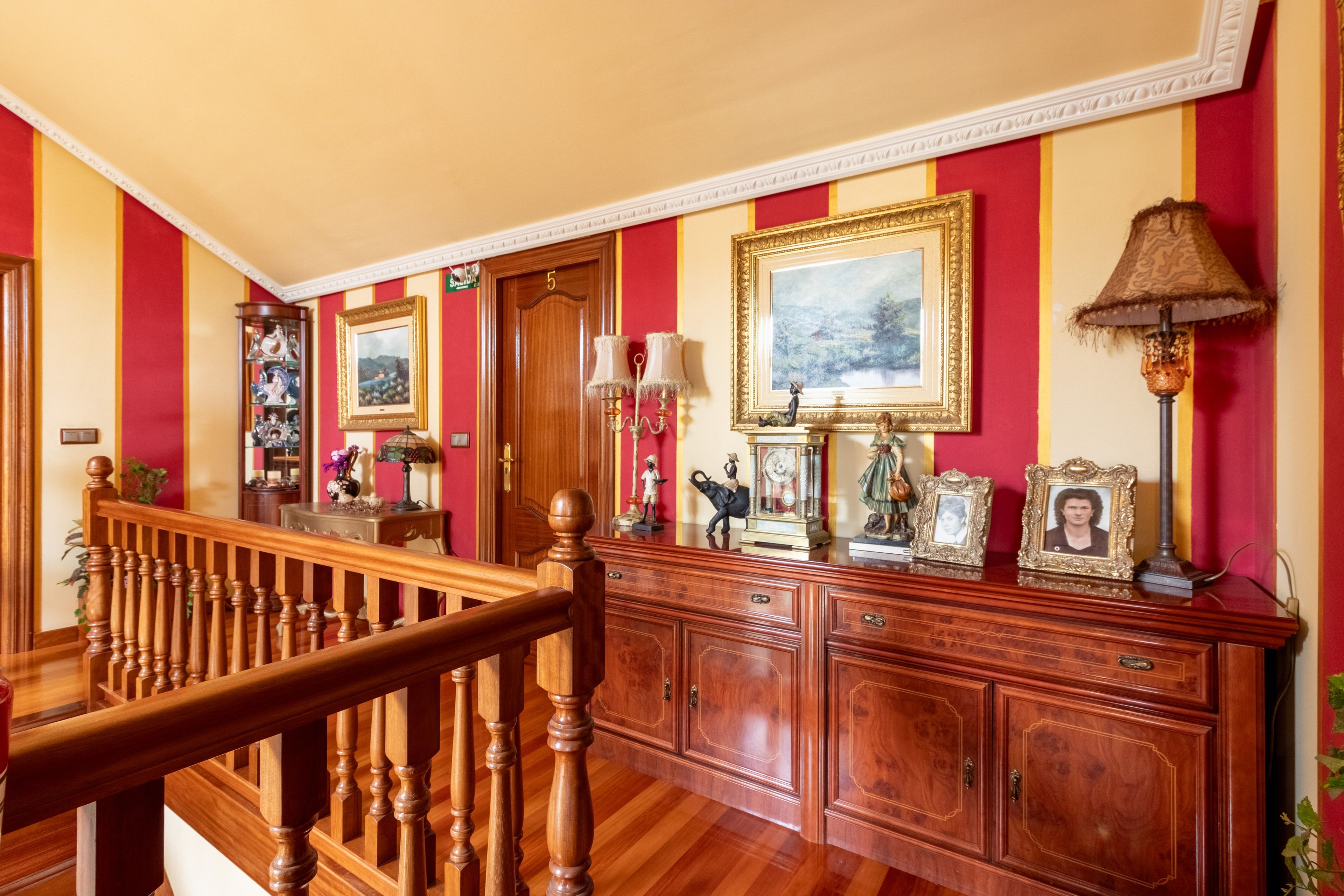 Um amplo corredor com escadaria de madeira, um grande armário de madeira com várias gavetas e uma porta com o número 5.