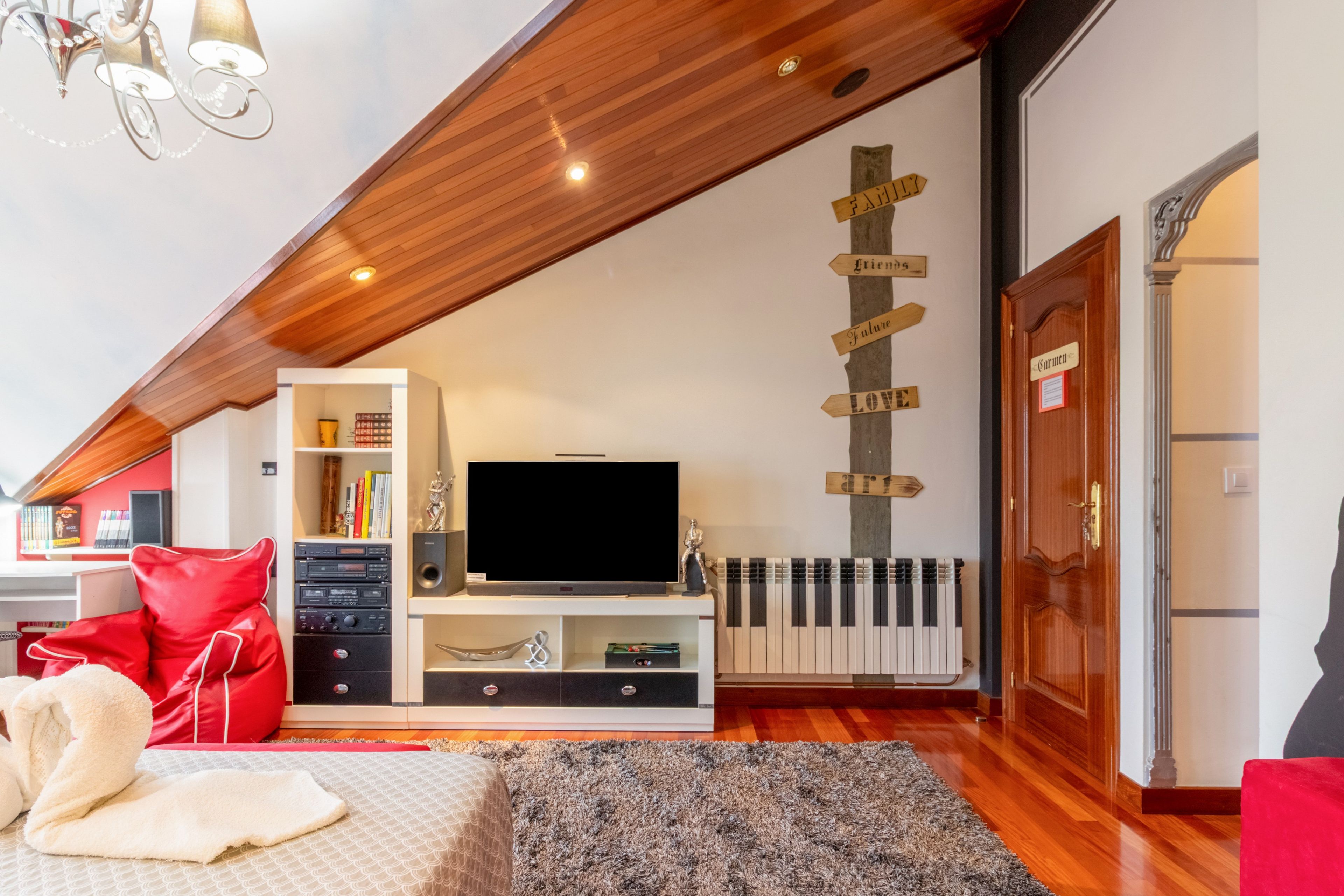 A modern living room with a flat-screen TV, a bookshelf, a red sofa, and a decorative wall with wooden signs.
