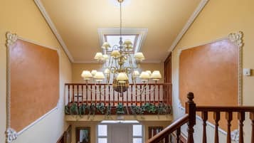 A grand staircase with a chandelier, a balcony with greenery, and a door at the bottom.