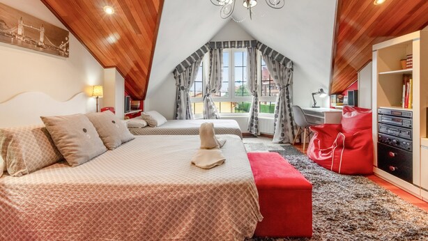 Une chambre avec deux lits, un pouf rouge, un lustre et une vue sur l’extérieur.