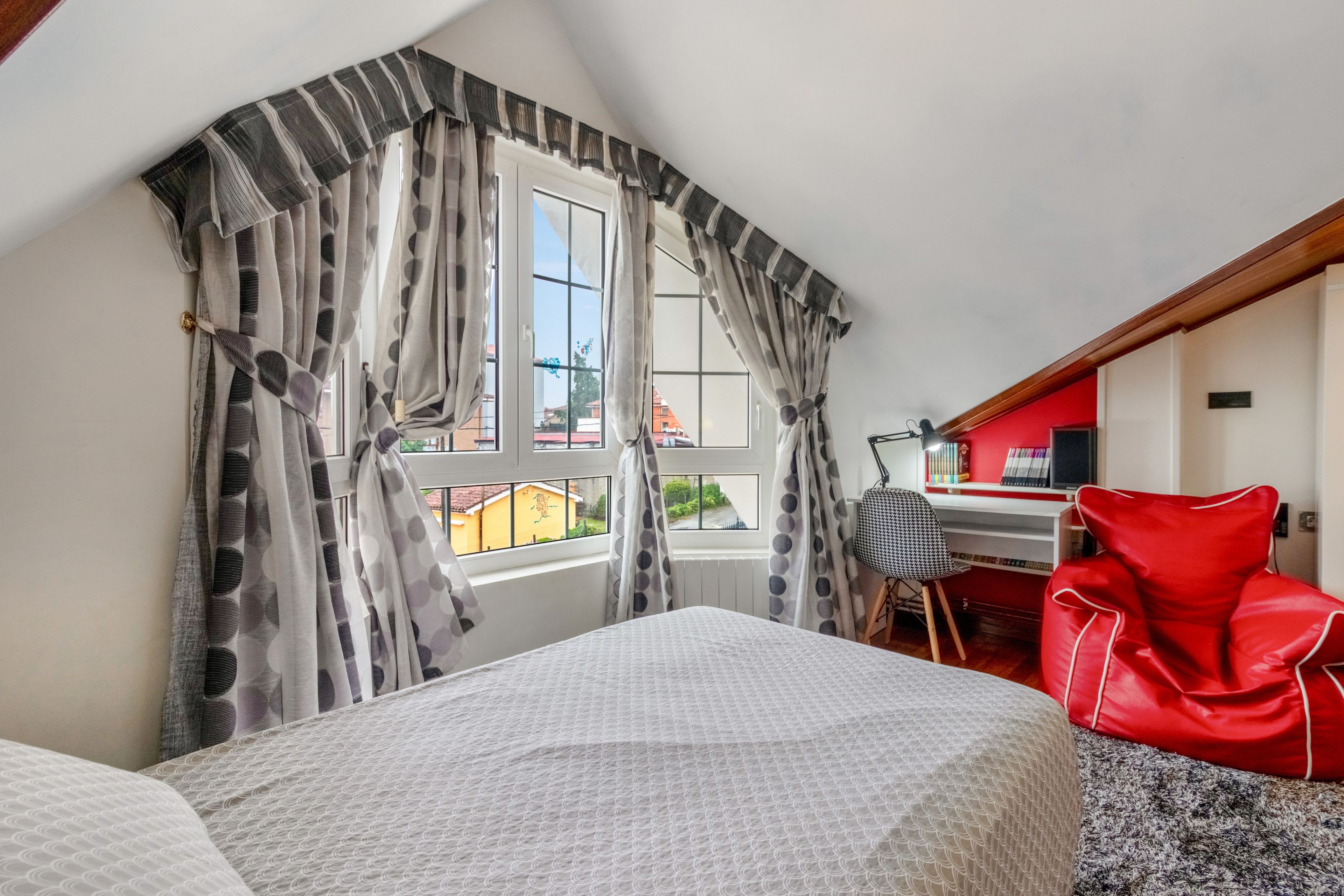 A bedroom with a bed, a desk, and a chair. There is a window with curtains.