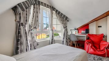 A bedroom with a bed, a desk, and a chair. There is a window with curtains.