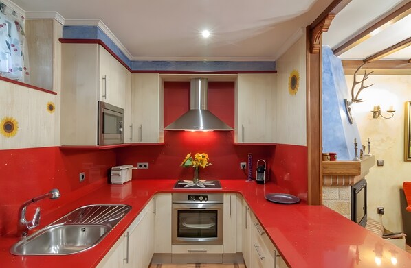 A kitchen with a red countertop, stainless steel appliances, and a central island with a vase of flowers.