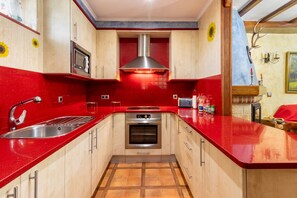 A kitchen with red countertops, a stainless steel sink, a microwave, an oven, and a range hood.