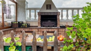Une cuisine extérieure en briques, dotée d’un barbecue, entourée d’une clôture en bois, et un balcon avec une balustrade.