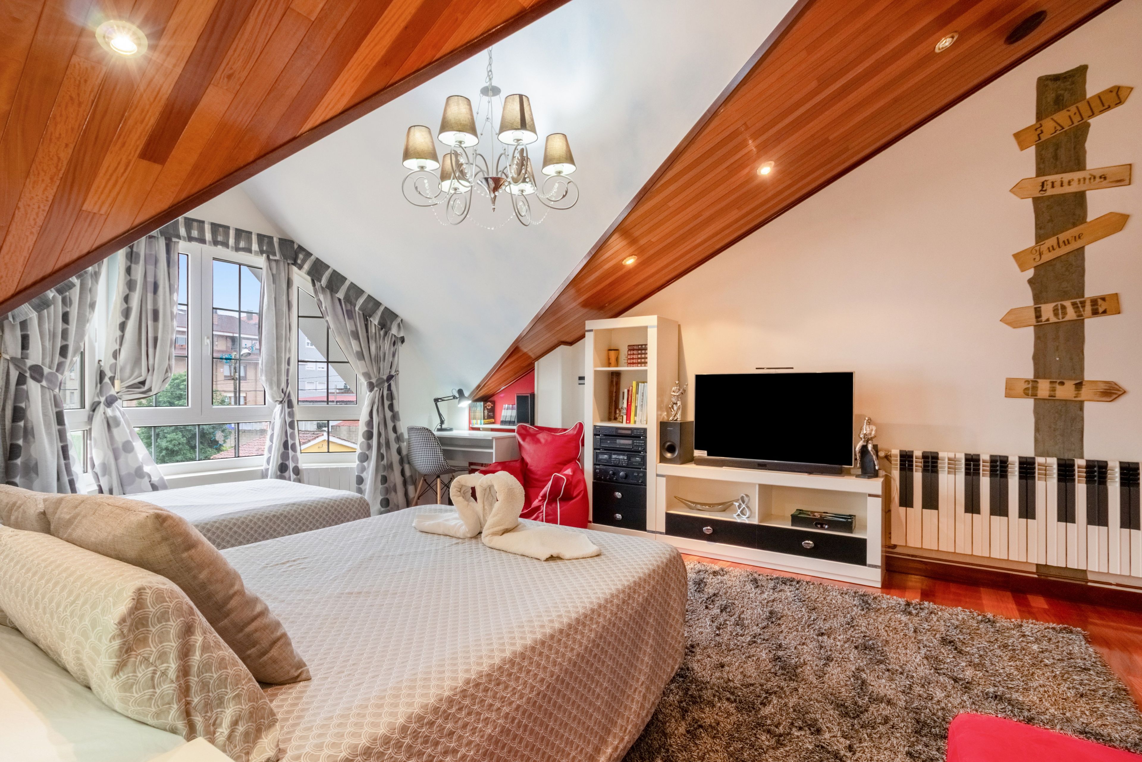Ein Schlafzimmer mit schrägen Wänden, einer Chandelierleuchtreibe, einem Bett mit Handtuch, einem Fernseher, einem Klavier und einer Wand mit Hinweisschildern.