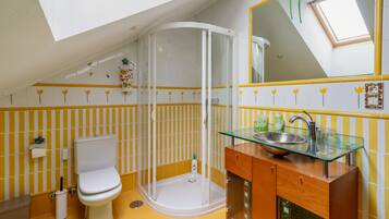 Un baño con cabina de ducha de vidrio, inodoro y lavamanos con encimera de cristal.