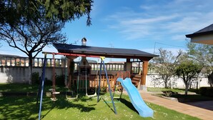 Un parque infantil con columpios, tobogán y una casita de juegos cubierta.
