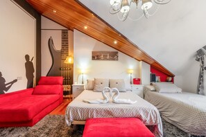 A bedroom with a sloped ceiling, a bed with two pillows, a red chair, a bench, and a wall-mounted guitar.
