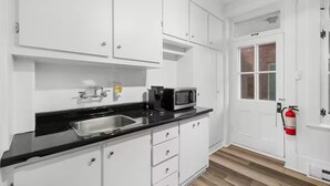 A kitchen with white cabinets, a black countertop, a sink, a microwave, and a fire extinguisher. - Perfect Location! Perfect Stay in Quebec City!
Suite Jardin (Québec)