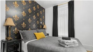 A bedroom with a bed, two bedside tables, a lamp, a window with curtains, and a wall with a pattern. - Perfect Location! Perfect Stay in Quebec City!
Suite Jardin (Québec)