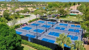 Ein Tennisplatzkomplex mit mehreren Plätzen, umgeben von Grünflächen und einem Poolbereich.