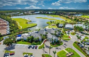 Vista aérea de un campo de golf con un gran estanque, rodeado de edificios residenciales y un estacionamiento.