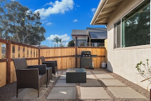 Un patio con mobiliario exterior, una parrilla y vistas a una casa.
