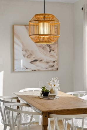 Un comedor con una mesa de madera, sillas blancas, una lámpara colgante y una obra de arte de mármol en la pared.
