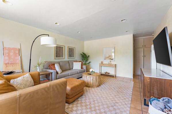 Un salon moderne comprenant un canapé, un pouf, une table basse et un téléviseur à écran plat.