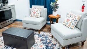A living room with two armchairs, a coffee table, and a sofa. There is a small side table with a plant and a fire extinguisher on the wall. - Hyland Suite 103, Hyland Hotel (Palmer)