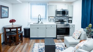 A compact kitchen with white cabinets, a microwave, and an oven. There's a dining table with chairs and a small trash bin. - Hyland Suite 103, Hyland Hotel (Palmer)