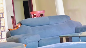 Un salon avec un canapé bleu, une chaise en bois et un pilier blanc.