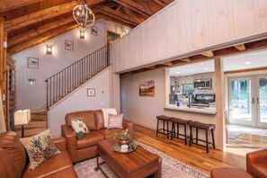 A spacious living area with a wooden ceiling, a staircase, a kitchen with a bar, and a large window. - Rocky Top Ridge - Private Modern Log Cabin Retreat on Lake (Loudon)