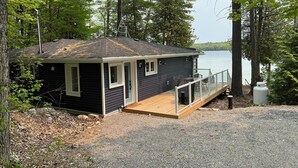 A small cabin with a deck and a dock extending into a lake, surrounded by trees. - Beautiful Sandy Lake Cabin (as seen on HGTV) (Trent Lakes)