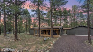 A cabin with a porch, a garage, and a gravel driveway surrounded by trees. - Charming Pines Cabin / Fireplace + BBQ Retreat (Show Low)