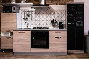 A modern kitchen with wooden cabinets, a built-in oven, a microwave, and a chalkboard with a welcome message.