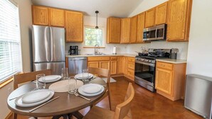 A modern kitchen with wooden cabinets, stainless steel appliances, and a dining area set for four. - Quiet/New 2bd Suite w/ Laundry, Kitchen, Wi-Fi (Palmer)