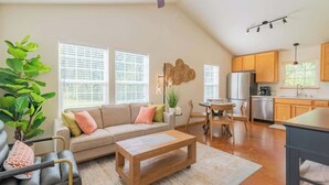 A spacious living area with a sofa, coffee table, and dining table. A kitchen with wooden cabinets and a refrigerator is visible in the background. - Quiet/New 2bd Suite w/ Laundry, Kitchen, Wi-Fi (Palmer)