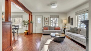 A living room with hardwood floors, a sofa, a coffee table, and a dining area with chairs and a table. - Hot Tub w/ Mt Views, Full Kitchen, Laundry (Palmer)