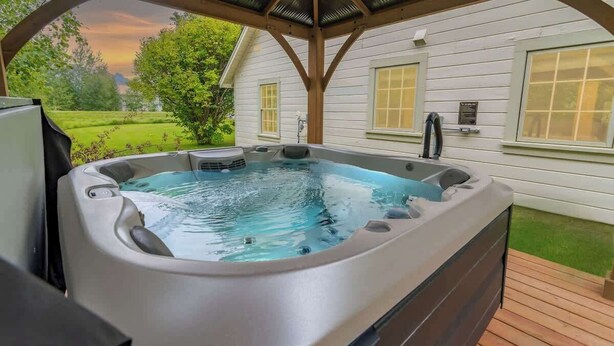 A hot tub in a covered outdoor area with a view of a house and greenery. - Hot Tub w/ Mt Views, Full Kitchen, Laundry (Palmer)