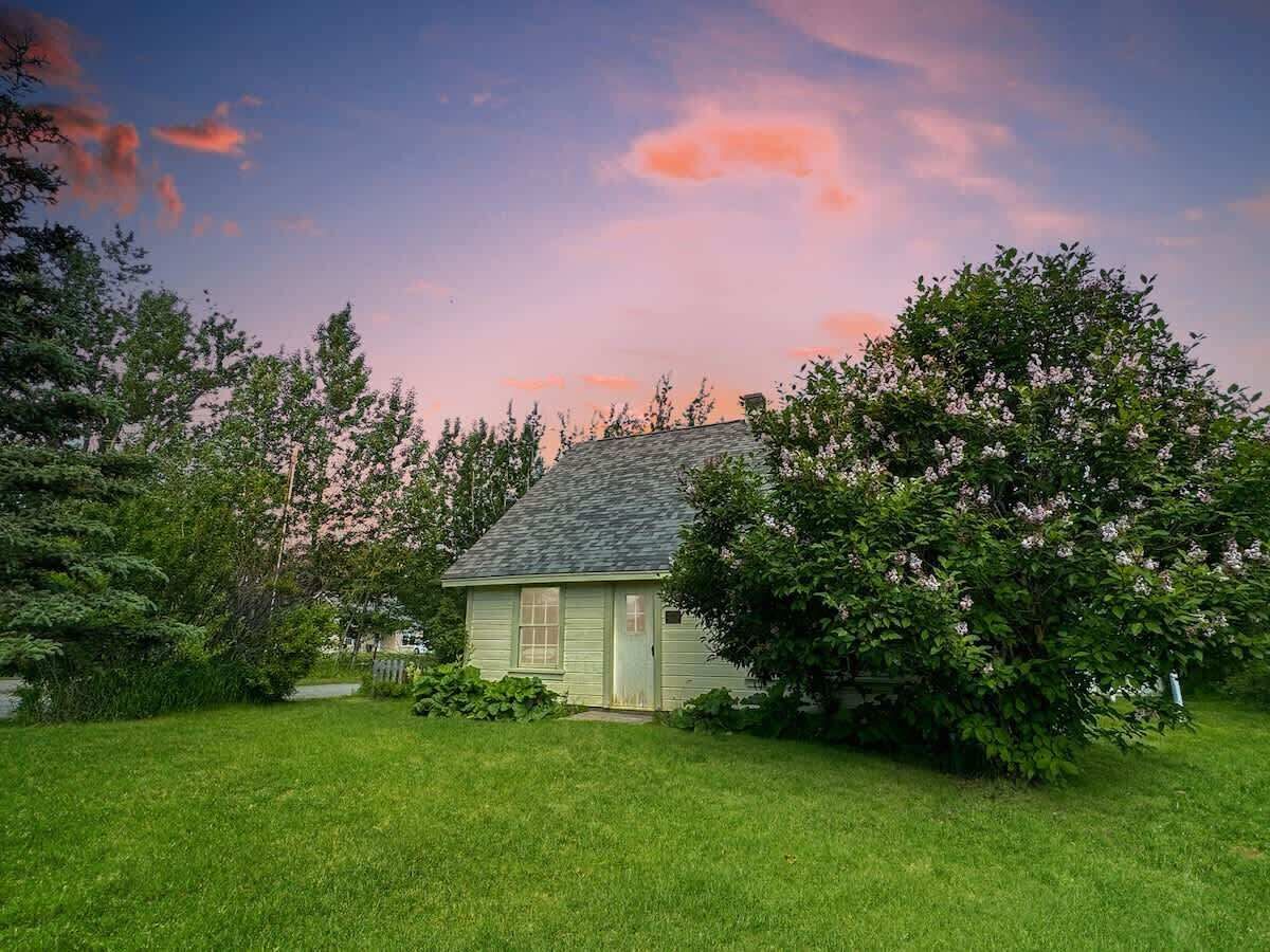 A small house with a sloped roof, surrounded by a well-maintained lawn and flowering trees.