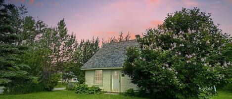 A small house with a sloped roof, surrounded by a well-maintained lawn and flowering trees.