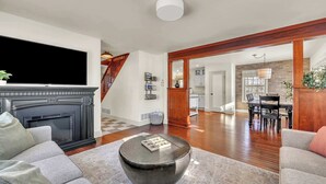 A spacious living room with a fireplace, a television, a round coffee table, and a dining area in the background. - Hot Tub w/ Mt Views, Full Kitchen, Laundry (Palmer)