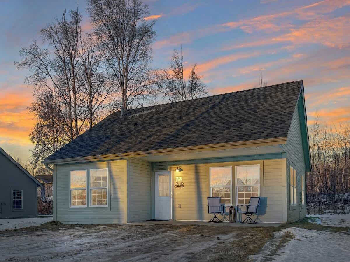 Une maison de plain-pied avec un toit en pente, un porche à l’avant doté de deux chaises et une porte de garage.