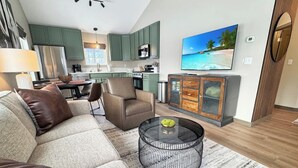 A modern living room with a sectional sofa, a round coffee table, and a TV mounted on the wall.