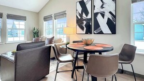 A modern living room with a sofa, chairs, a dining table, and abstract art on the wall.
