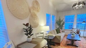 A living room with a dining area, featuring a round table, white chairs, a sofa, and a coffee table. There are large woven wall decorations, a floor lamp, and a potted plant. - Private & Quiet! 2bd/2ba w/ Laundry & Mt. Views! (Palmer)