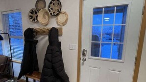 A room with a white door, a bench, and a coat rack with two coats. There are wall decorations and a window with blinds. - Private & Quiet! 2bd/2ba w/ Laundry & Mt. Views! (Palmer)